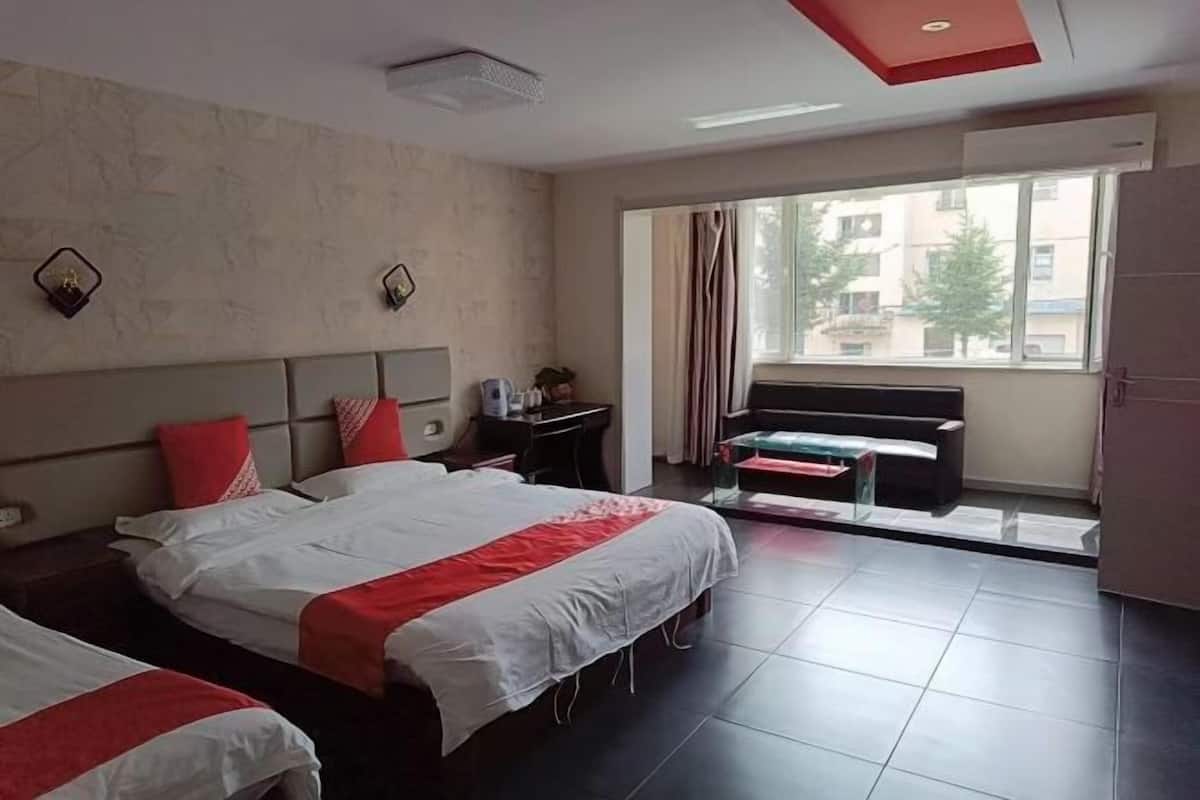 Habitación de hotel con dos camas, un escritorio, una silla, una ventana con cortinas y vistas a edificios.