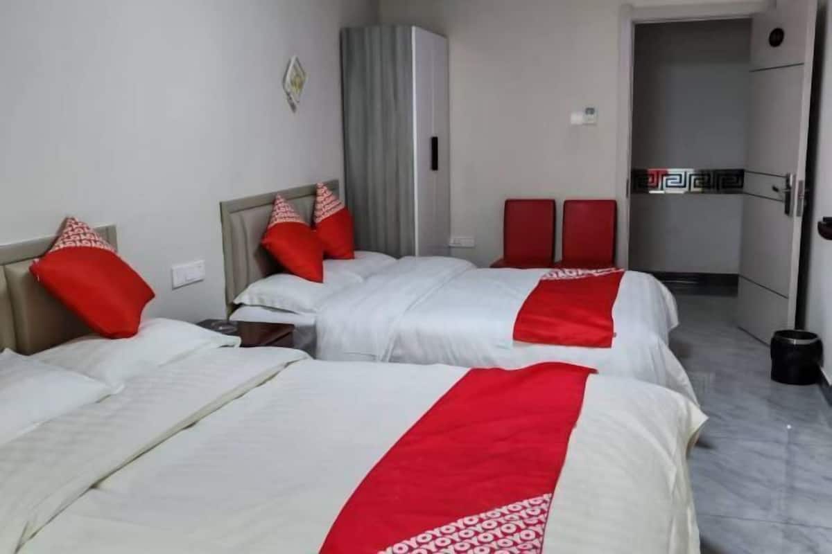 Habitación de hotel con dos camas, ropa de cama roja y blanca, un armario y una silla roja.