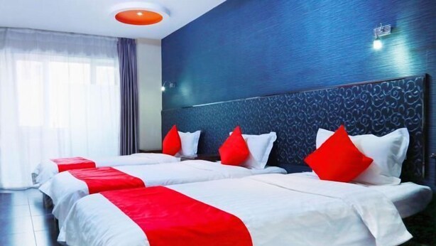 Ein Hotelzimmer mit zwei Betten, jeweils mit weißer Bettwäsche und roten Akzenten, einer dunkelblauen strukturierten Wand und einer modernen Deckenleuchte.