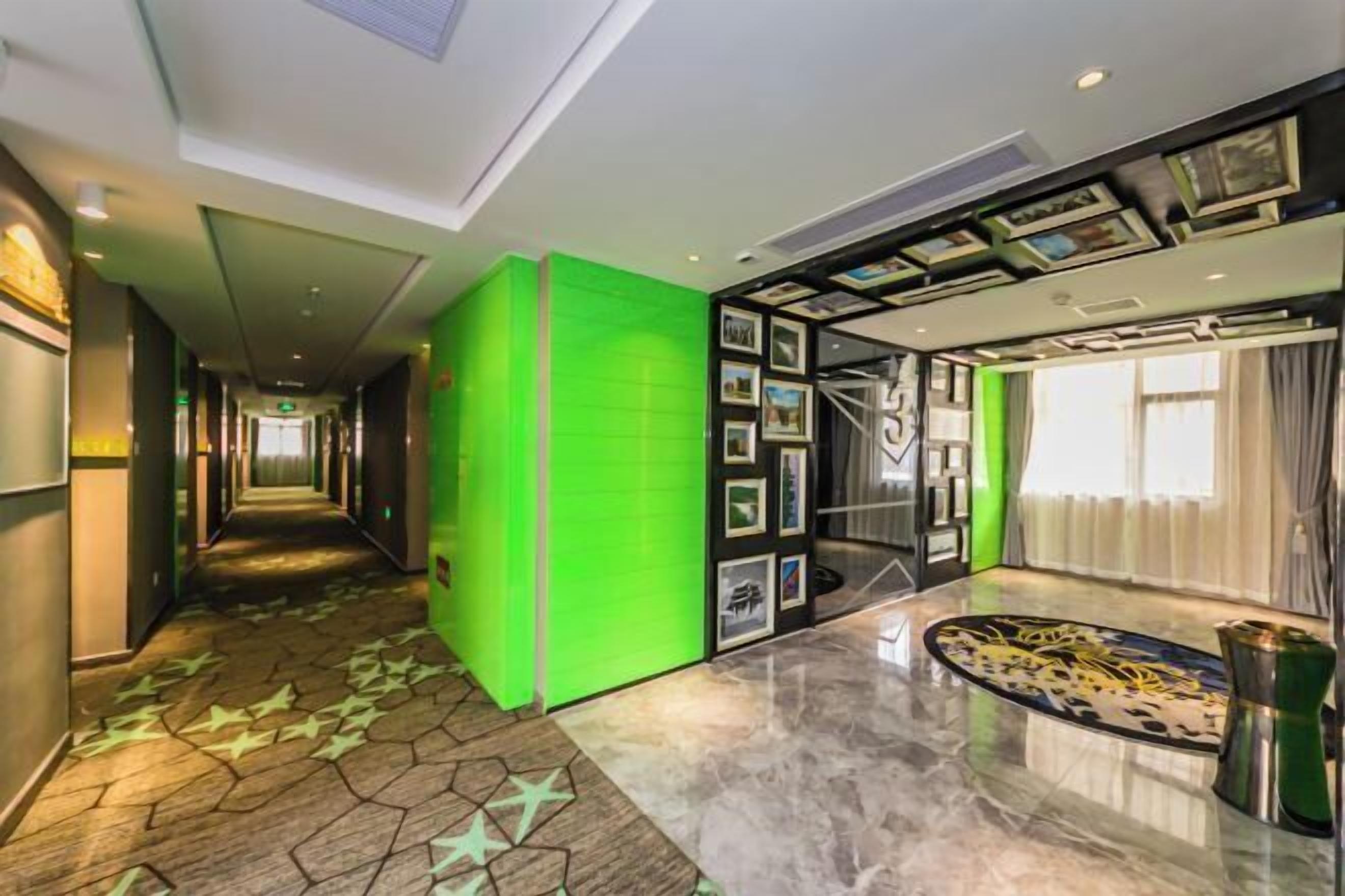 A hotel lobby with a long corridor, a green accent wall, framed pictures, a marble floor, and a decorative table.
