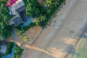 Vue aérienne d’une propriété située en bord de mer, avec un bâtiment, des palmiers et une plage de sable.