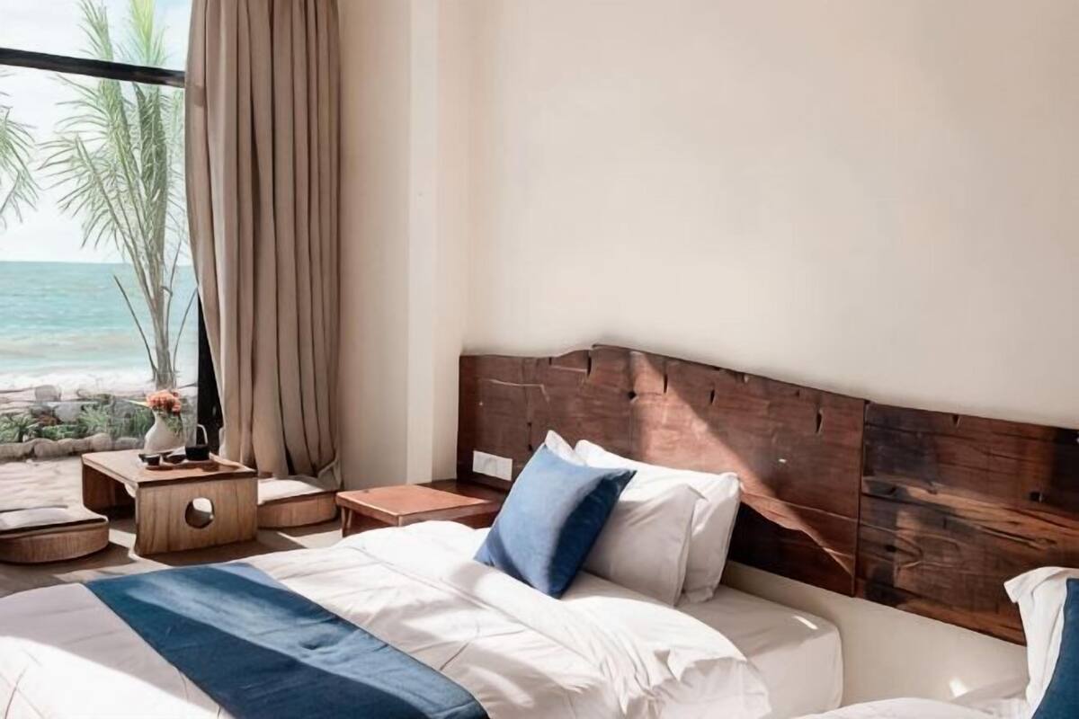 Une chambre d’hôtel avec un grand lit, une tête de lit en bois, une table de chevet et une vue sur l’océan.
