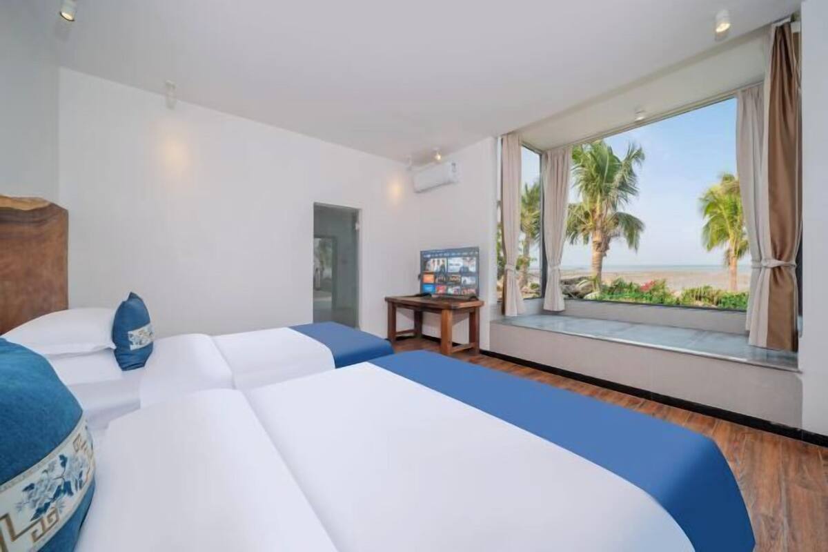 Une chambre d’hôtel avec deux lits, une télévision et une fenêtre donnant sur des palmiers et la plage.