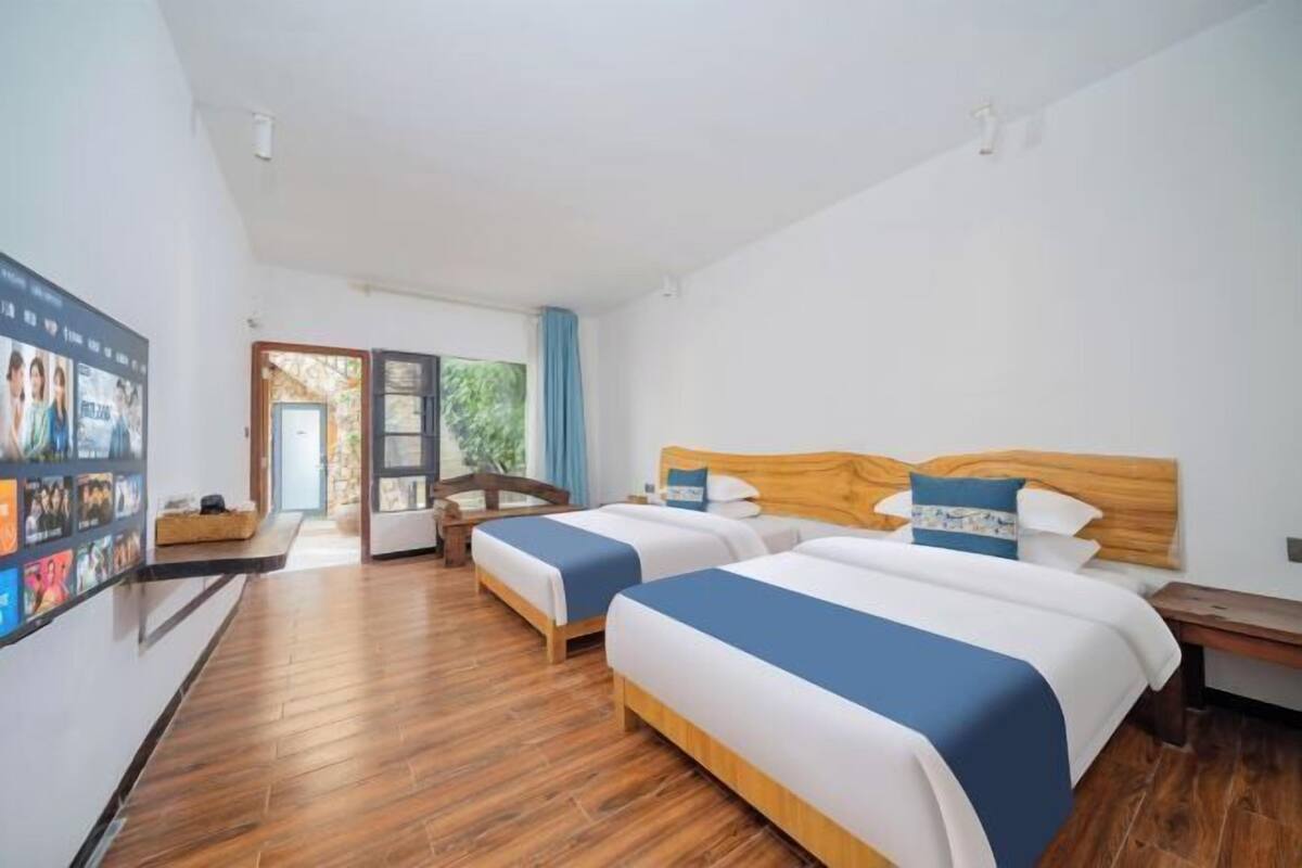 Une chambre d’hôtel avec deux lits, un plancher en bois, une télévision et une vue sur la verdure.