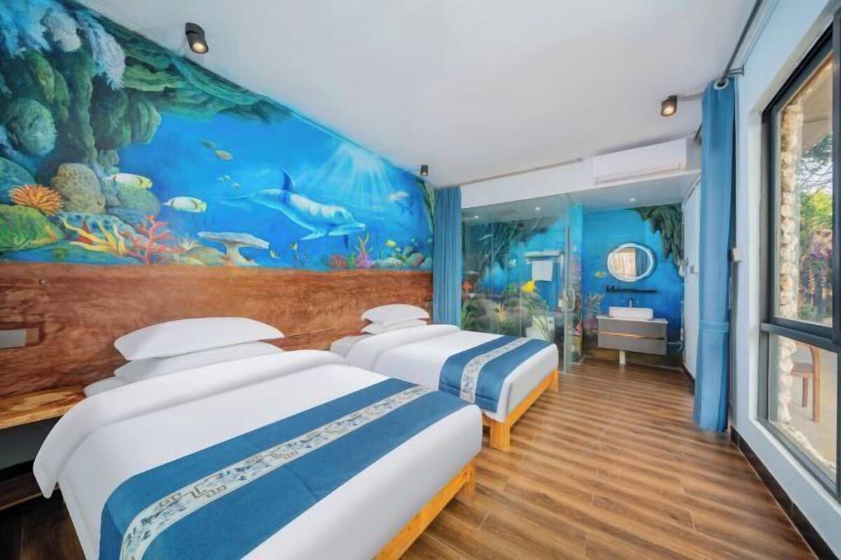 Une chambre avec deux lits, une fresque représentant une scène sous-marine, un plancher en bois et une grande fenêtre.