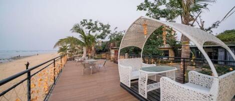 An outdoor deck with wicker furniture, a wooden floor, and a view of the beach.