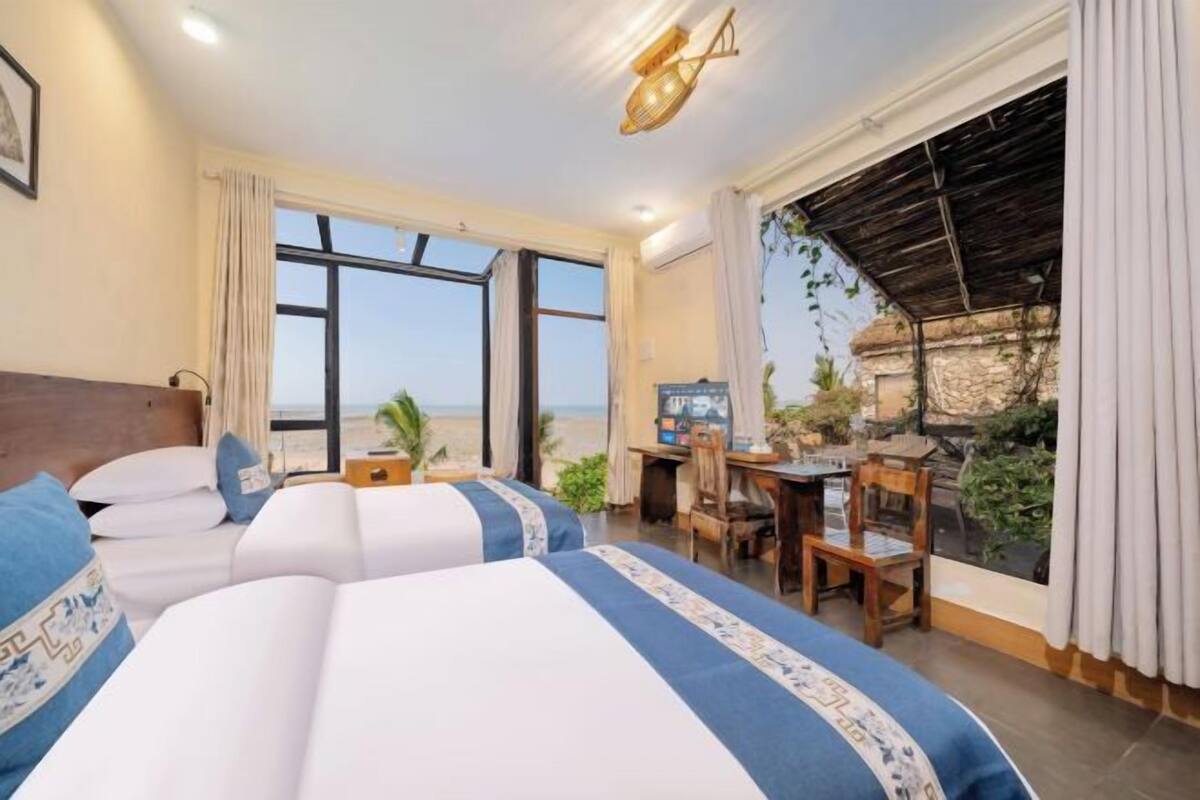 Une chambre d’hôtel avec deux lits, un bureau, une chaise et vue sur la plage.