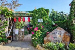 Een tuininloop met een houten poort, rode lantaarns en een steen met inscripties.