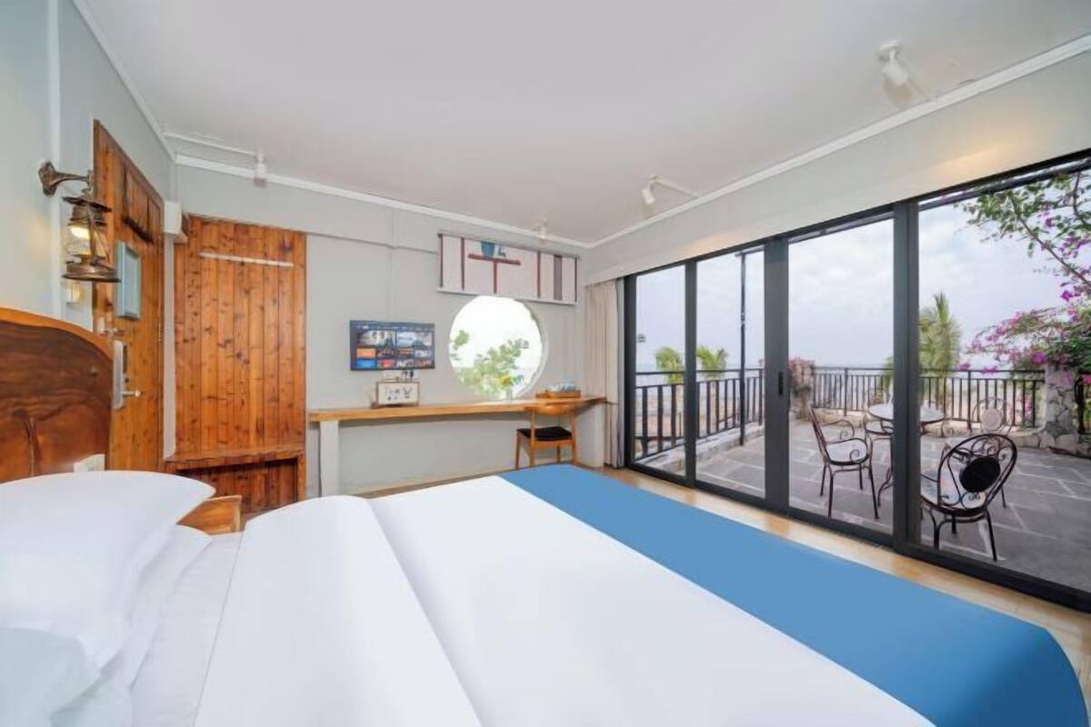 Une chambre dotée d’un grand lit, d’une armoire en bois, d’un bureau avec une chaise et d’un balcon avec des sièges d’extérieur.