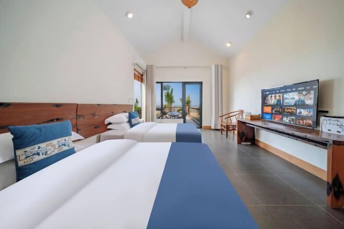 Quarto de hotel com duas camas, televisão e varanda com vista.