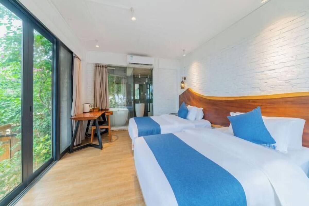 Une chambre d’hôtel avec deux lits, une tête de lit en bois, un bureau et une grande fenêtre.