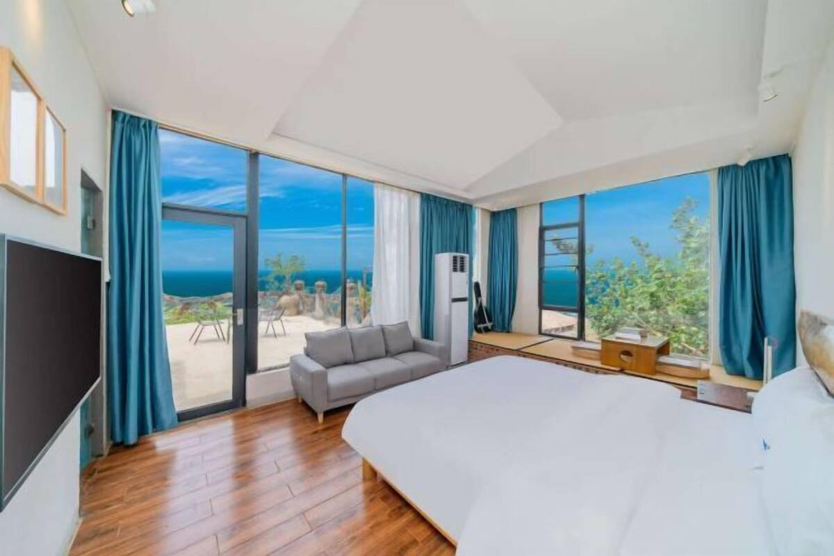 Une chambre d’hôtel moderne dotée d’un grand lit, d’une télévision, d’un balcon avec vue sur la mer et d’un coin salon avec une table et des chaises.