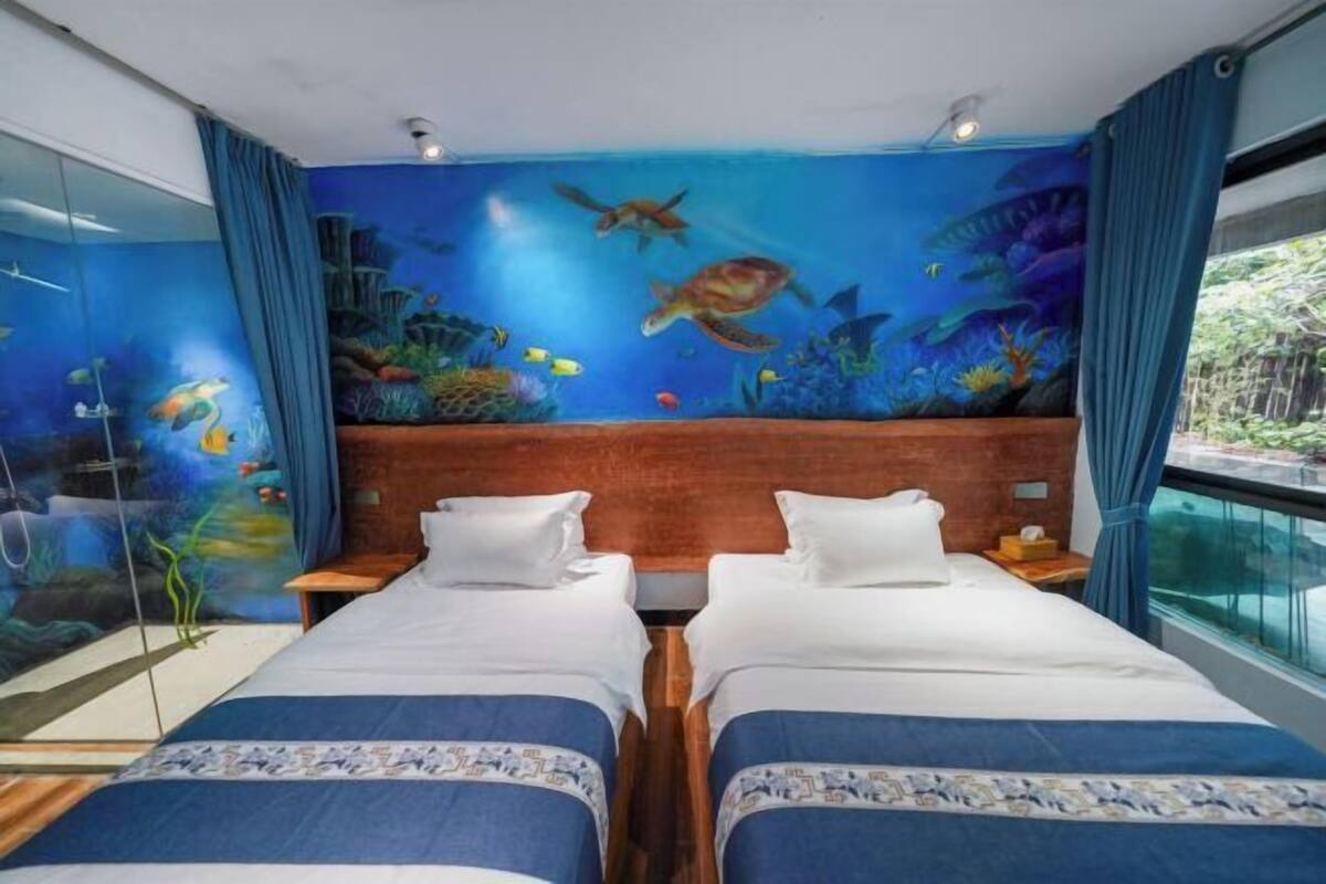 Une chambre avec deux lits, une fresque représentant une scène sous-marine et une fenêtre donnant sur un jardin.