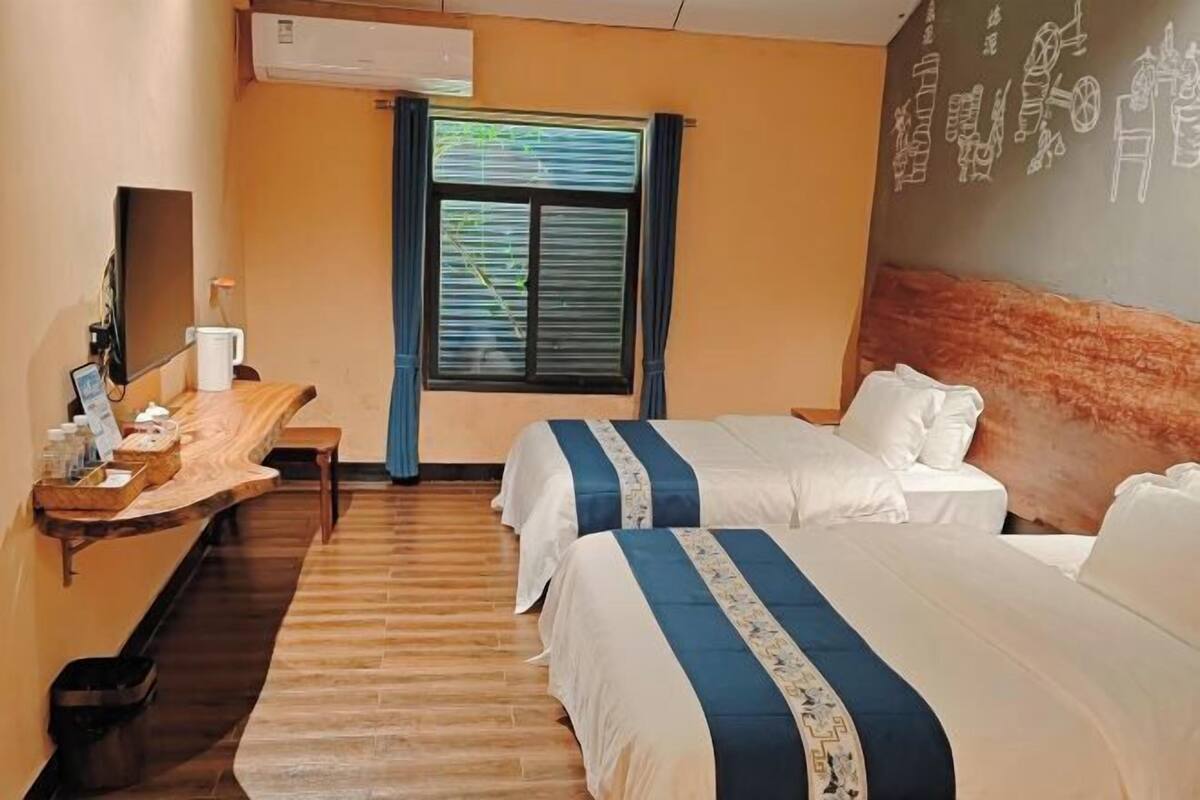 Une chambre d’hôtel avec deux lits, un bureau avec un ordinateur, une fenêtre avec des stores et un mur orné d’une fresque.