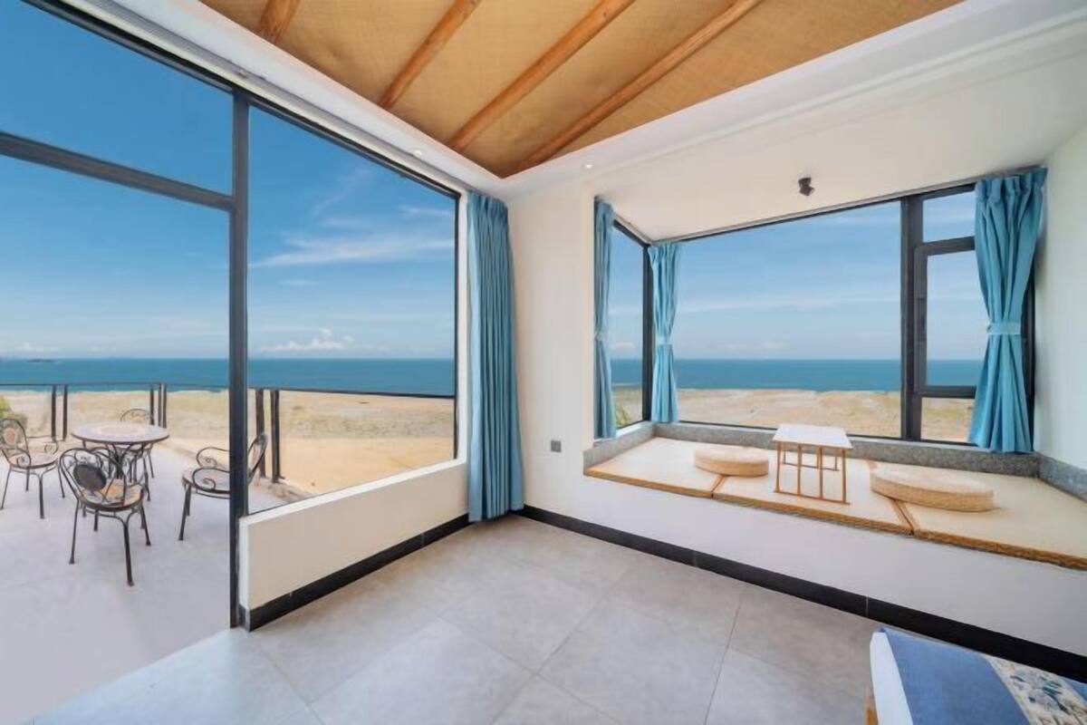 Une pièce dotée de grandes fenêtres, d’un balcon avec des chaises et d’un coin salon avec des coussins.