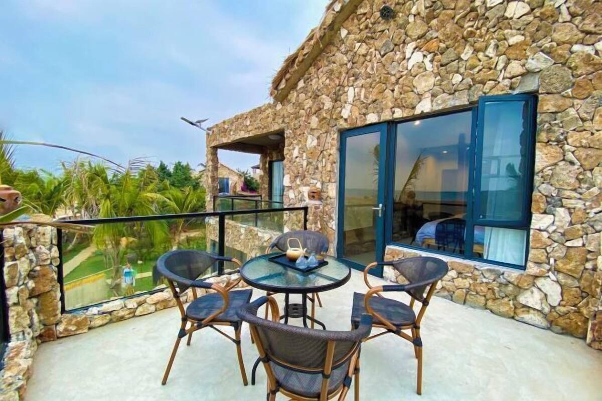 Un bâtiment en pierre avec une porte en verre, un balcon avec des chaises et une table sur laquelle se trouve un plateau.