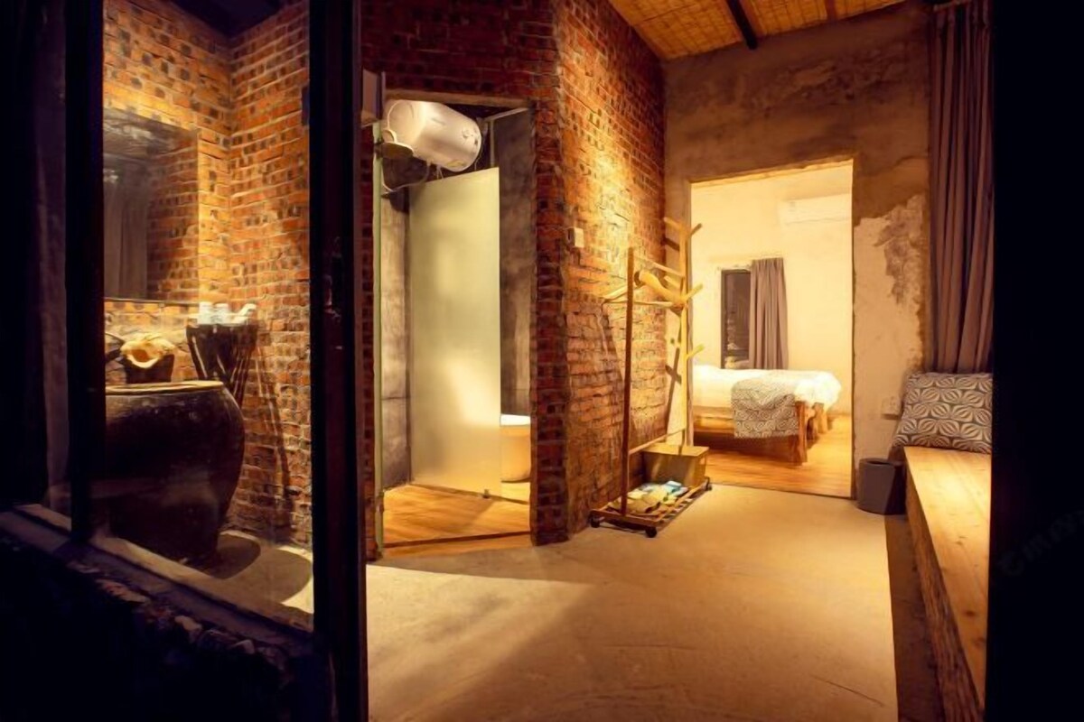 Una habitación rústica con paredes de ladrillo visto, una olla grande, una cama y un banco de madera.