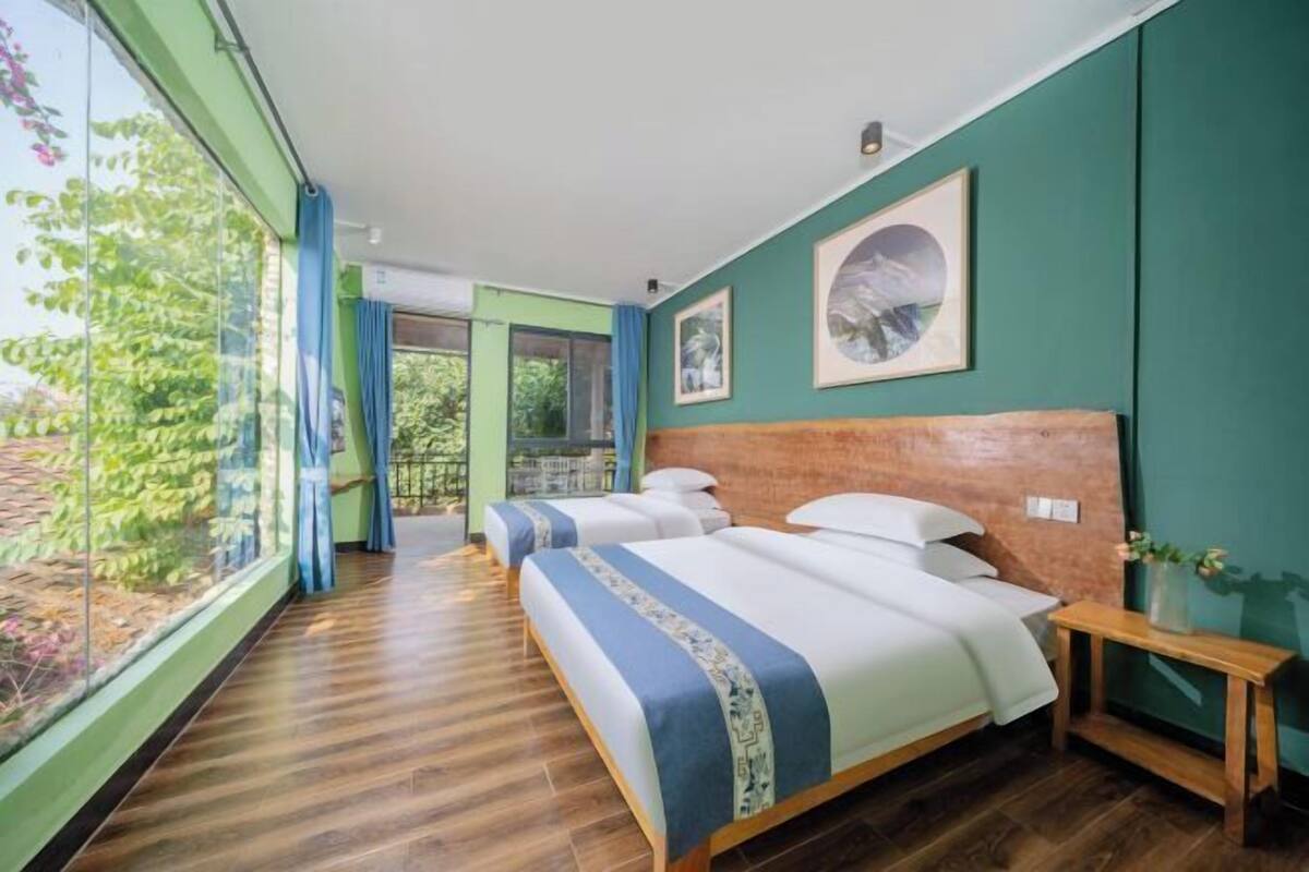 Une chambre d’hôtel avec deux lits, une grande fenêtre et une vue sur la verdure.