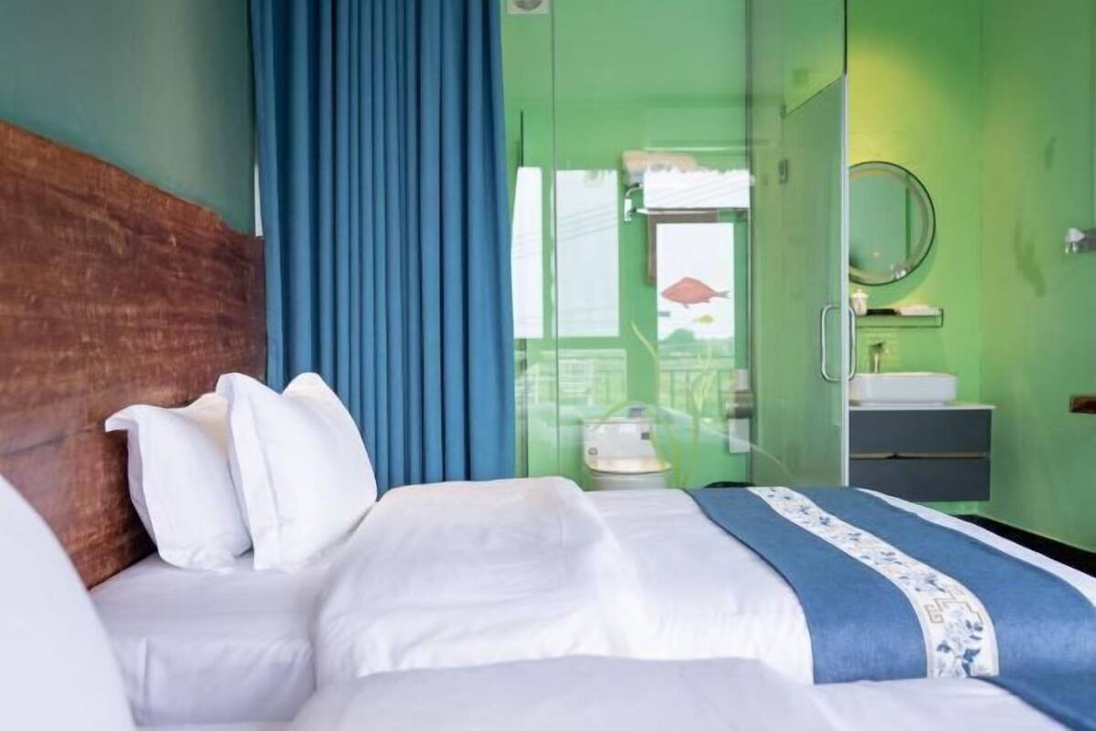 Une chambre d’hôtel avec un lit, une table de chevet, un miroir et une salle de bain visible à travers une porte ouverte.