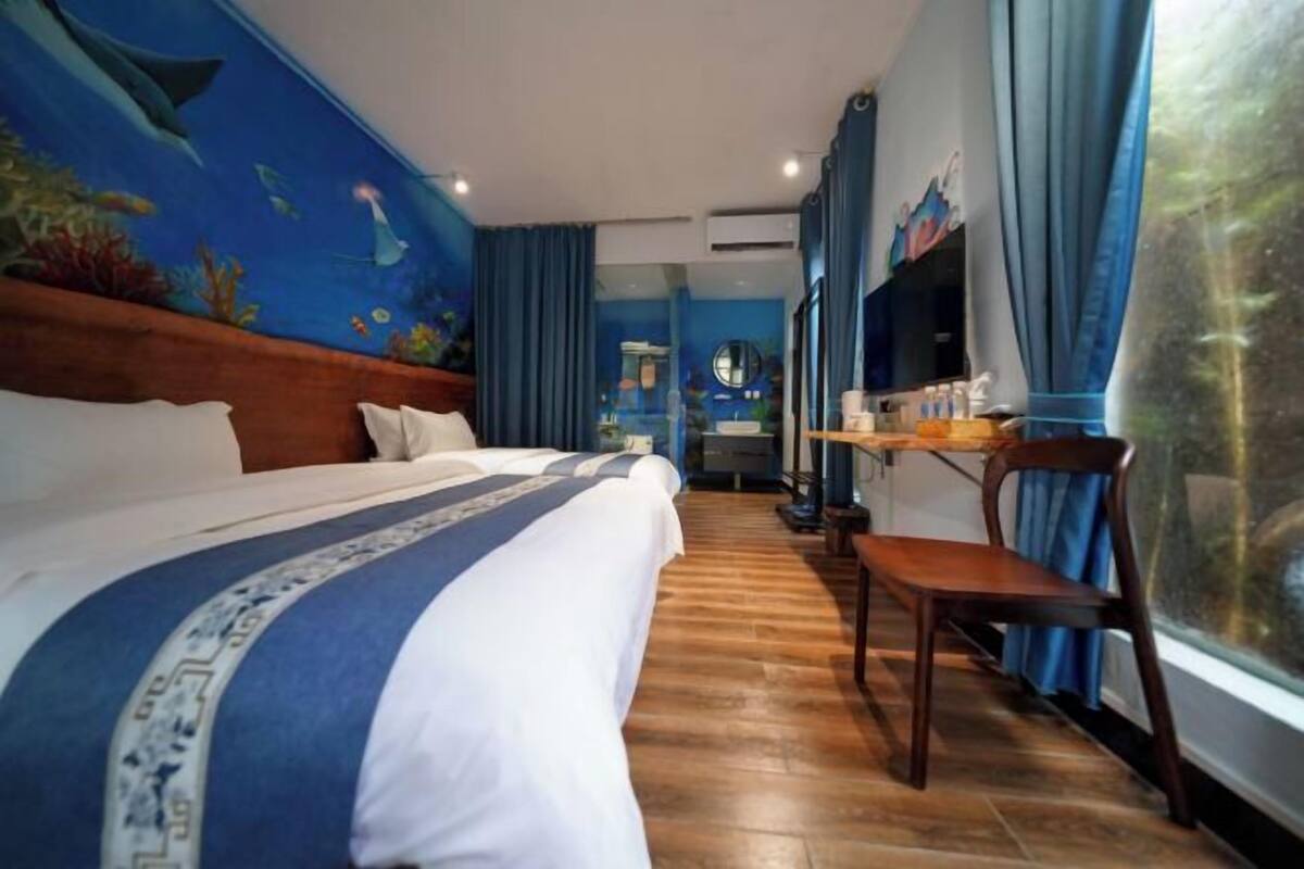 Une chambre d’hôtel avec un lit, un plancher en bois, un bureau avec une chaise, une télévision et une grande fenêtre avec des rideaux.