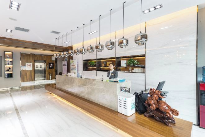 A modern hotel reception area with a marble counter, hanging pendant lights, and a wooden bench.