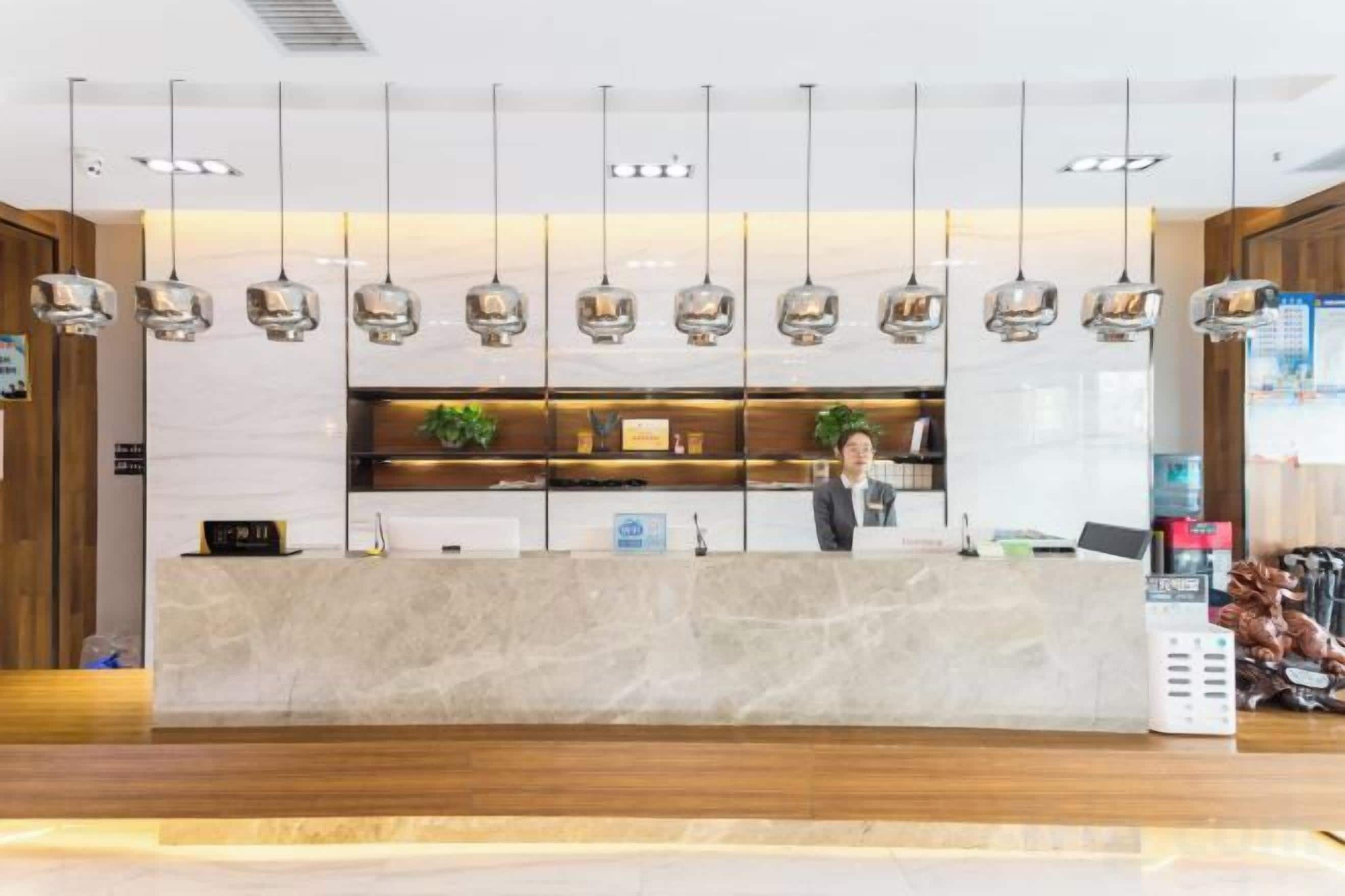 A hotel reception area with a marble counter, hanging pendant lights, and a receptionist.