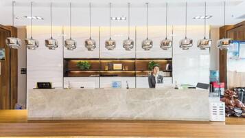 A hotel reception area with a marble counter, hanging pendant lights, and a receptionist.