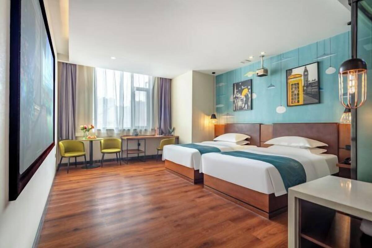 Een hotelkamer met twee bedden, een bureau, stoelen, een groot raam en kunst aan de muren.