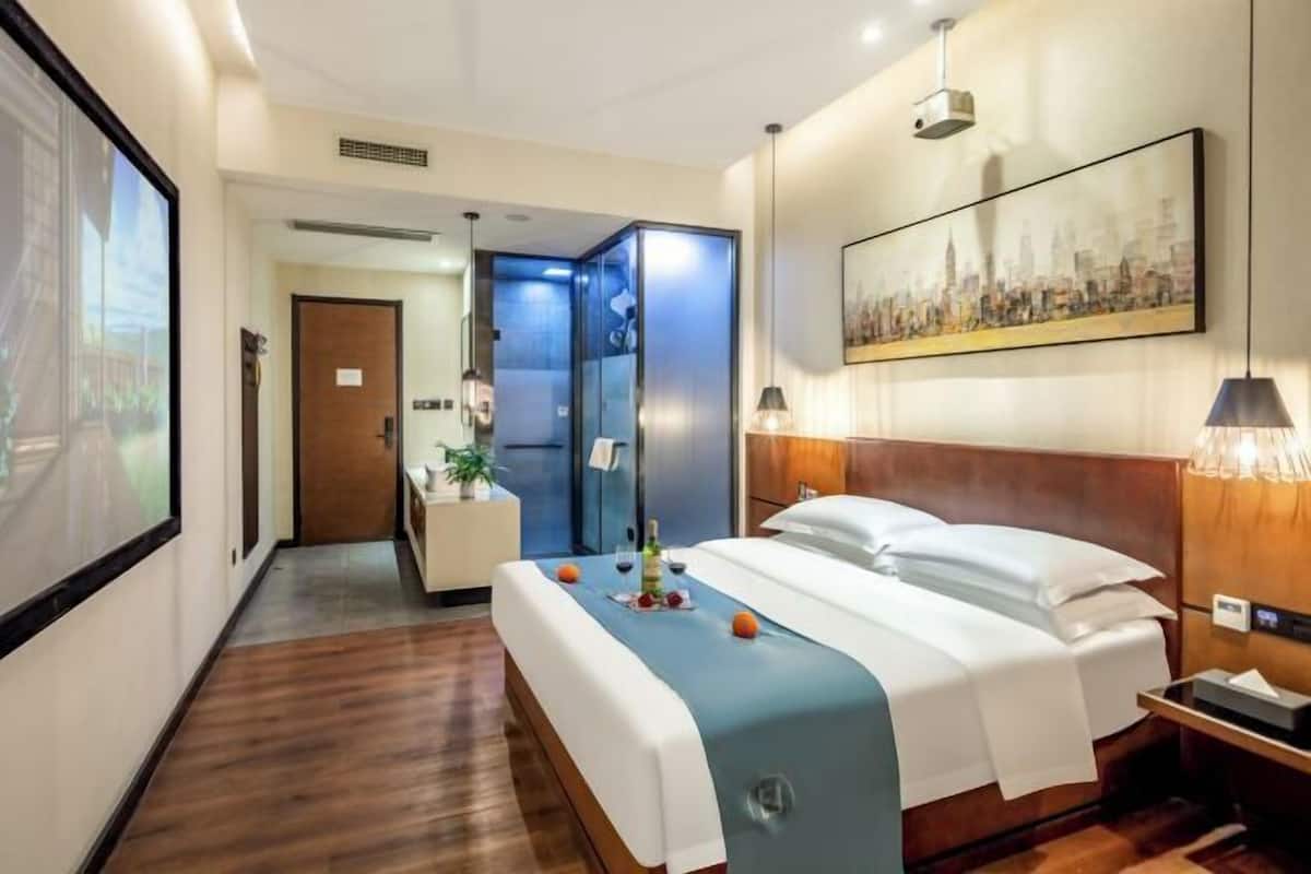 Een hotelkamer met een bed, nachtkastje, decoratie aan de muur en een gang naar de badkamer.