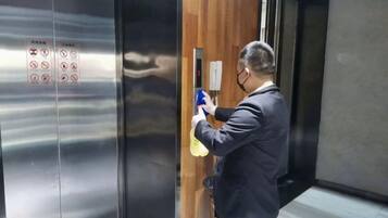 A person using a spray bottle in an elevator with a wooden panel and metallic surfaces.