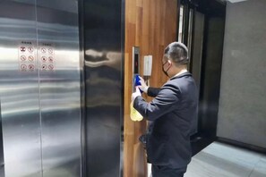 A person using a spray bottle in an elevator with a wooden panel and metallic surfaces.
