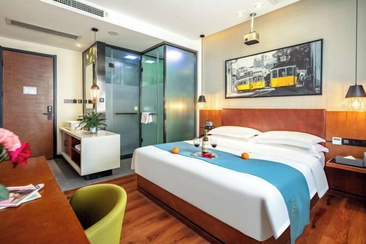 Een hotelkamer met een bed, nachtkastje, bureau, stoel en een schilderij aan de muur.