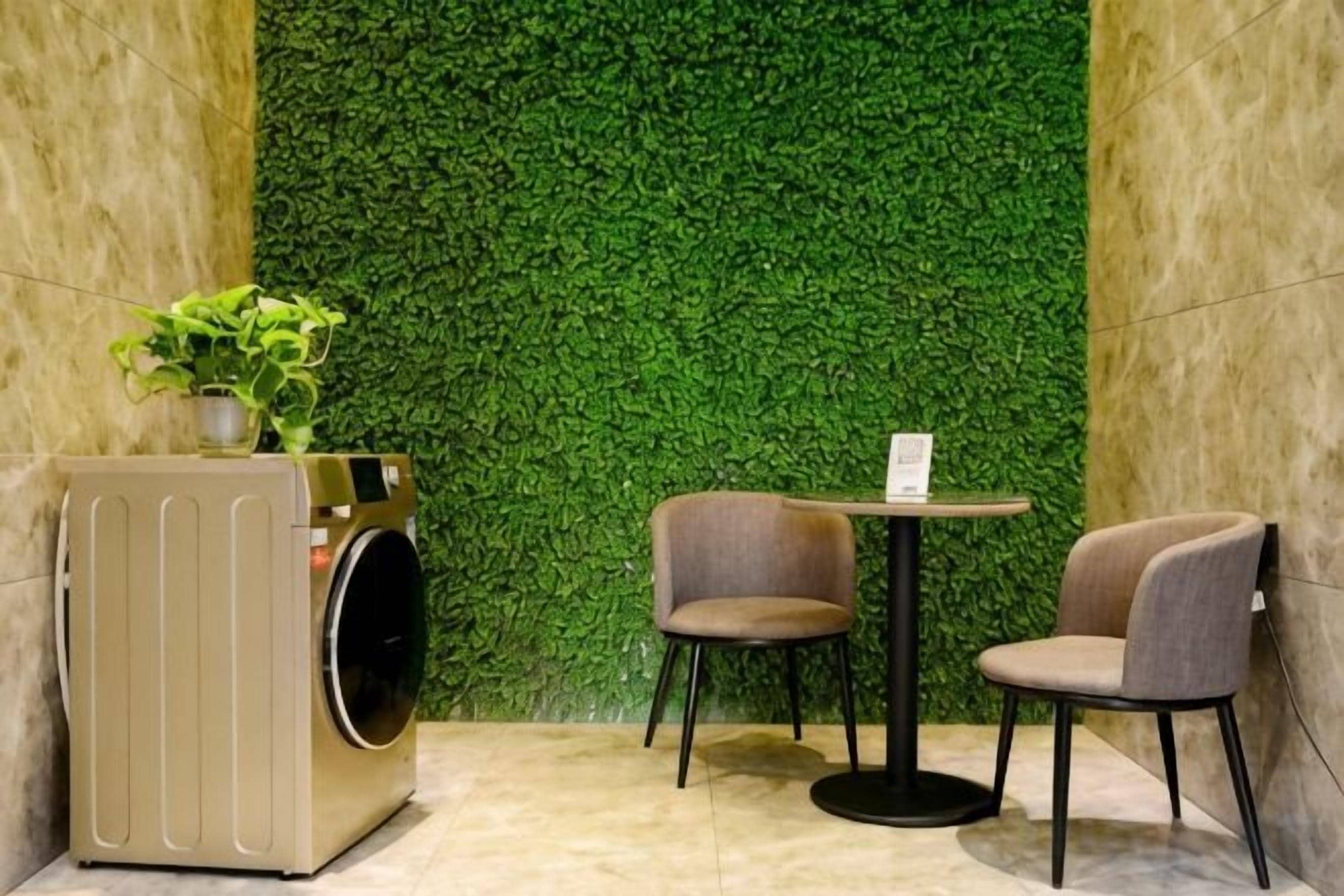 A room with a green wall, a washing machine, two chairs, and a small table.