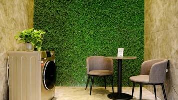 A room with a green wall, a washing machine, two chairs, and a small table.