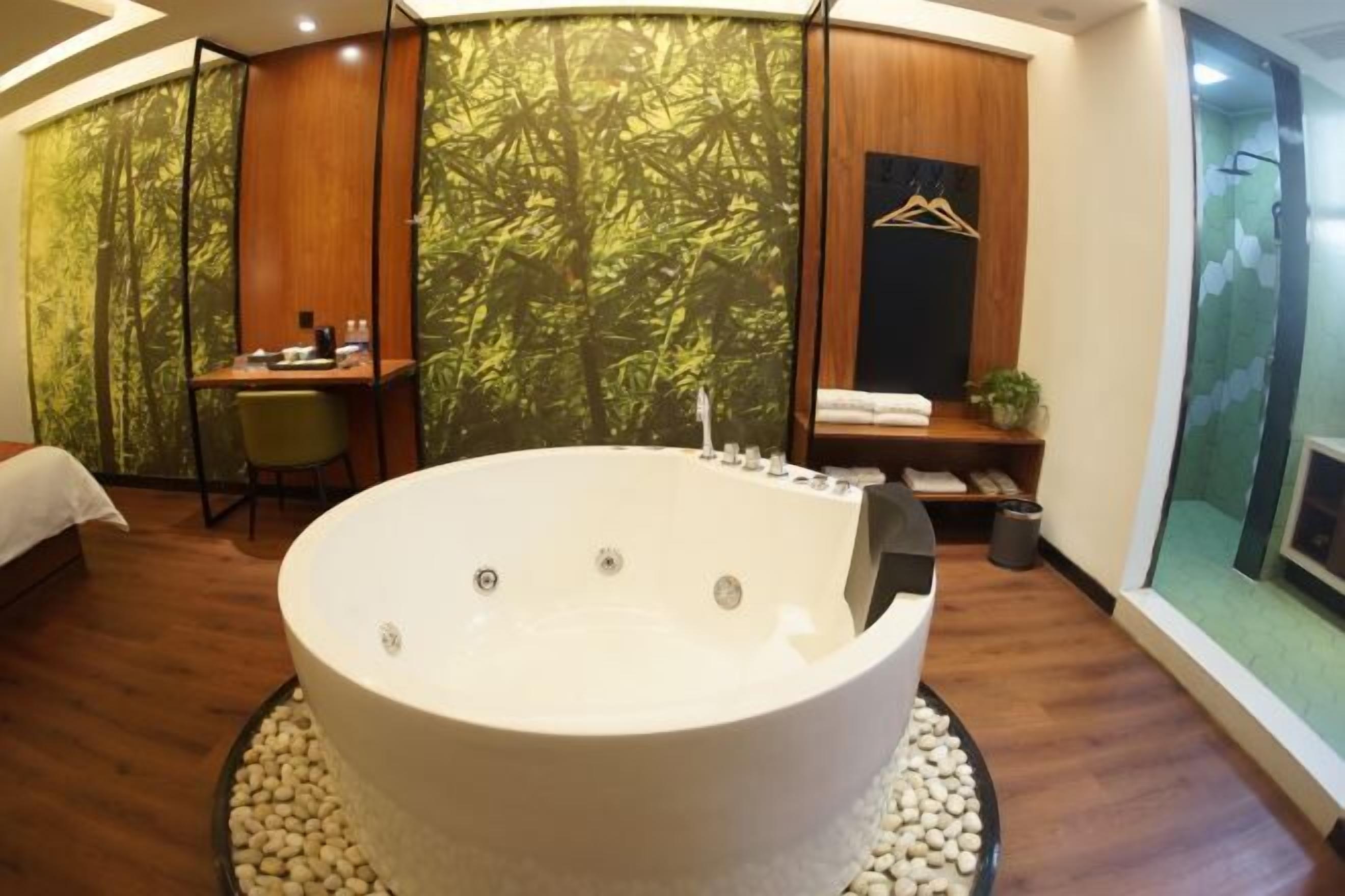 A modern bathroom with a large freestanding bathtub, a wooden desk, and a bamboo-themed wall.