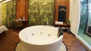 A modern bathroom with a large freestanding bathtub, a wooden desk, and a bamboo-themed wall.
