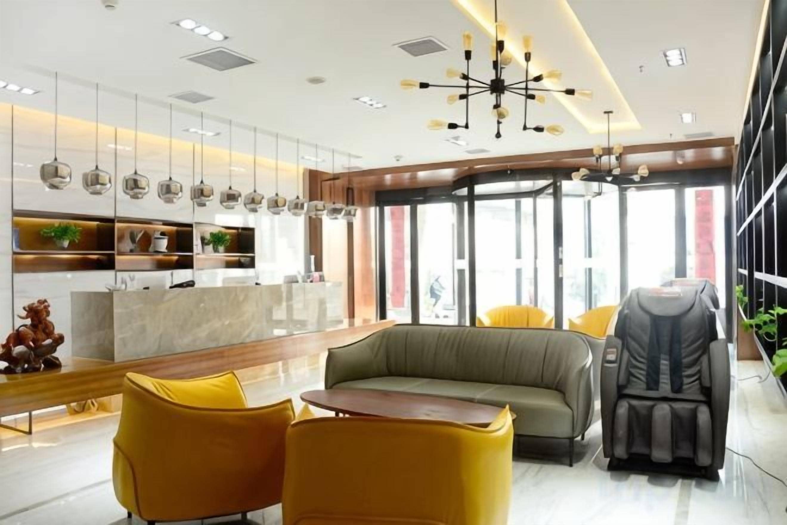 Un moderno vestíbulo de hotel con un mostrador de recepción, zona de estar, sillón de masaje y ventanas amplias.