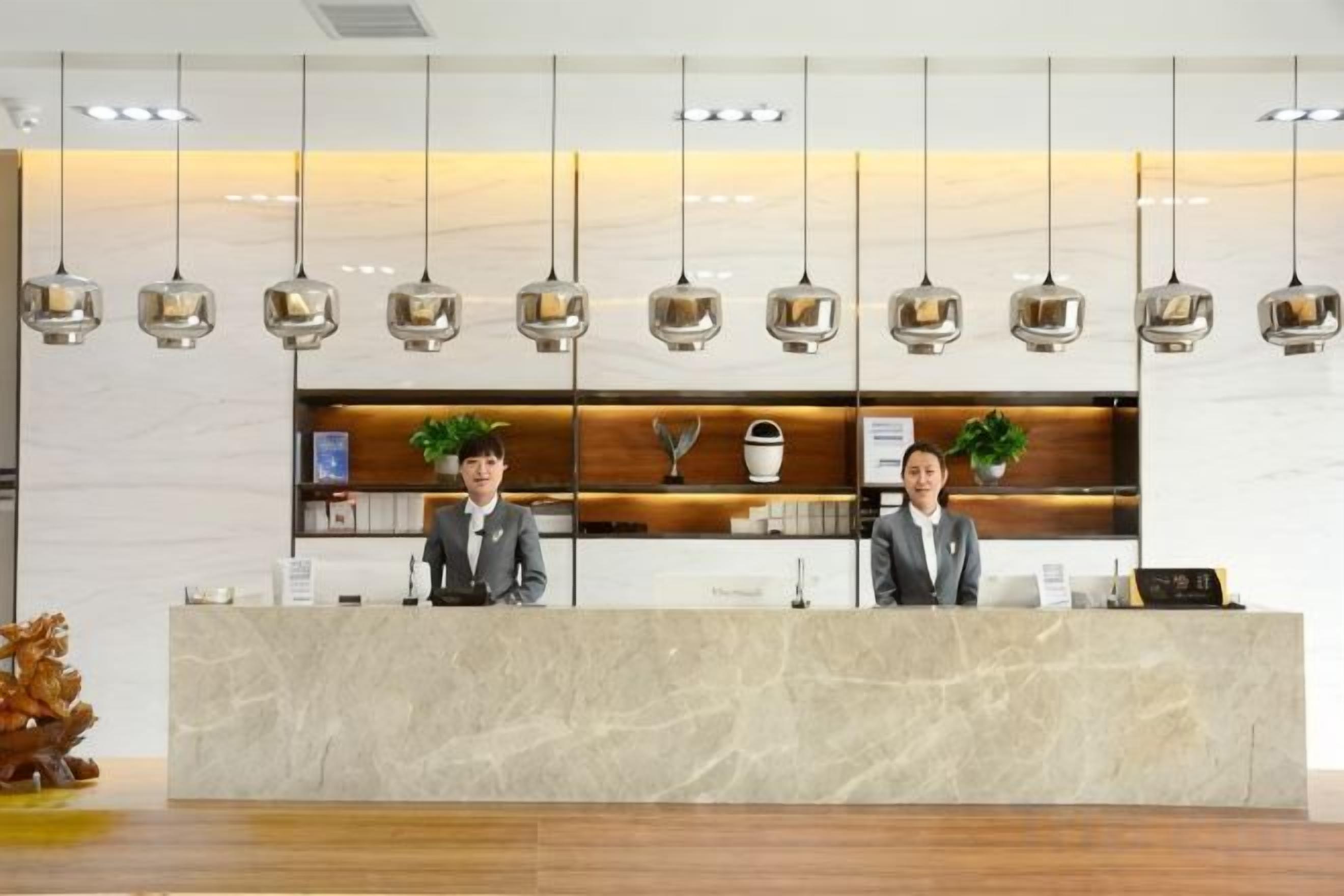 Een receptiebalie met twee medewerkers, een marmeren aanrecht en hangende pendelverlichting, plus een plantje op het aanrecht.