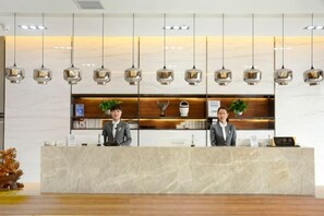 A reception desk with two staff members, a marble counter, hanging pendant lights, and a plant on the counter. - Yunpan Xiangyue hotel (Taiyuan)