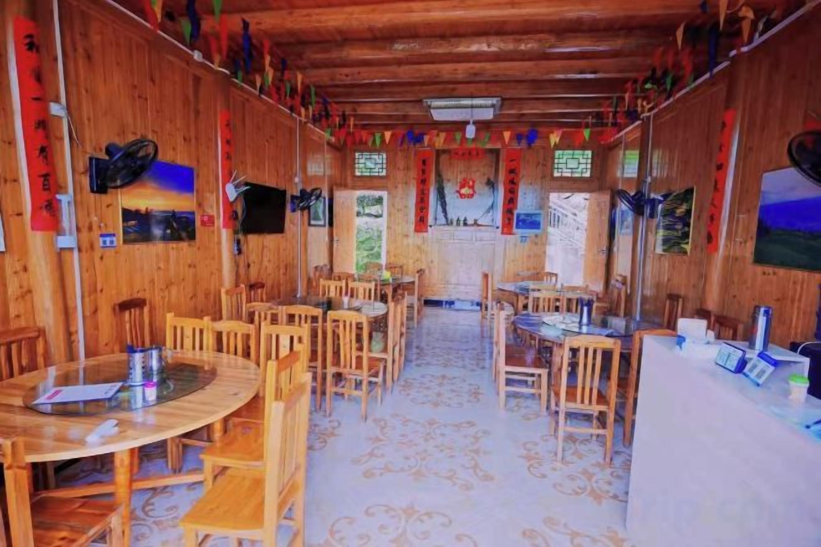 Un interior de madera con varias mesas y sillas, un suelo estampado y vistas a través de una ventana.