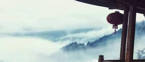 Une construction traditionnelle en bois, surmontée d’une lanterne rouge, qui offre une vue sur un paysage montagneux brumeux.
