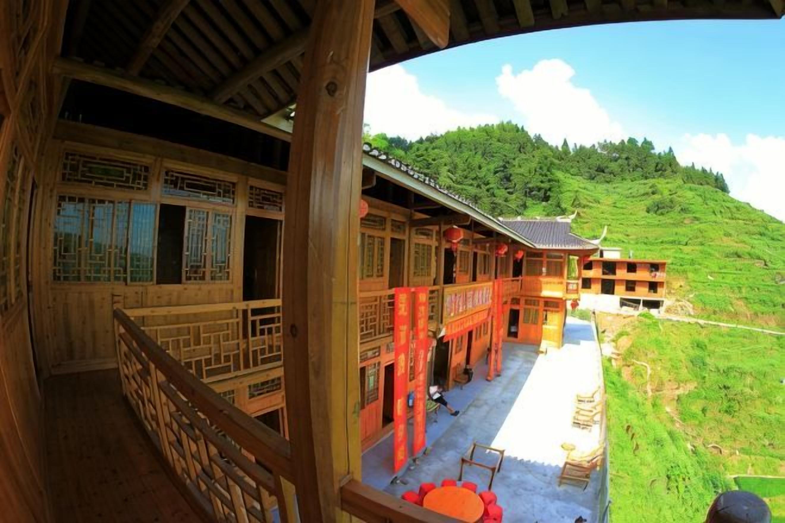A traditional wooden building with a balcony, a clear view of a green hillside, and a red lantern.