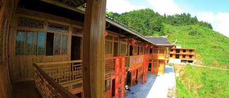A traditional wooden building with a balcony, a clear view of a green hillside, and a red lantern.