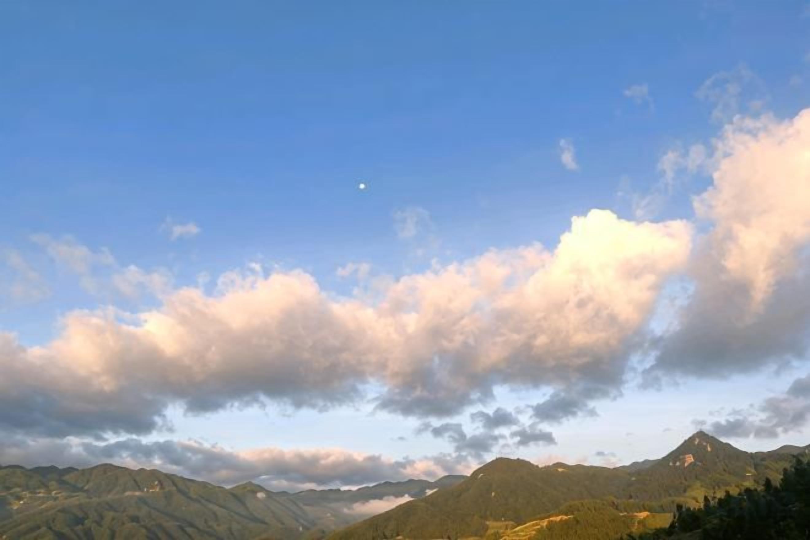 Un paysage montagneux, avec un ciel dégagé et une lune bien visible.