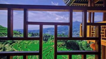 A view through a wooden lattice window of terraced green fields and distant mountains.