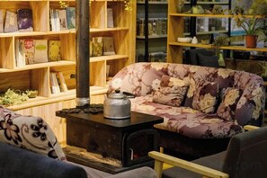 A cozy room with a floral sofa, a small table with a kettle, and wooden shelves filled with books and plants. - Dzongsa Book bar Inn (Shangri-La)