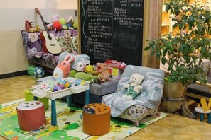 A cozy room with a sofa, a small table, a potted plant, and a chalkboard with writing. - Dzongsa Book bar Inn (Shangri-La)