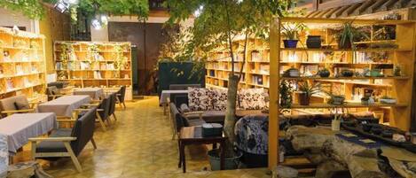 A cozy bookstore with wooden shelves, tables, and chairs, and a central seating area with a tree.