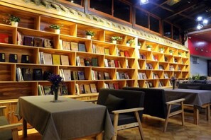 A bookstore with wooden shelves filled with books and small plants. There are tables with chairs for reading. - Dzongsa Book bar Inn (Shangri-La)