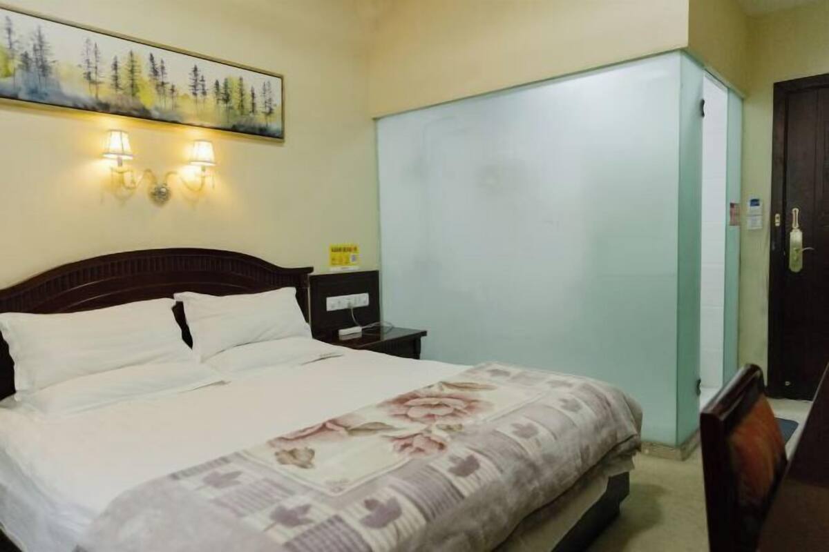 Una habitación de hotel con cama, mesita de noche, lámpara, armario y un cuadro en la pared.